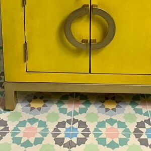 Fliesenboden mit Zementfliesen (Ausschnitt), auf dem der untere Teil eines gelben Schranks zu sehen ist