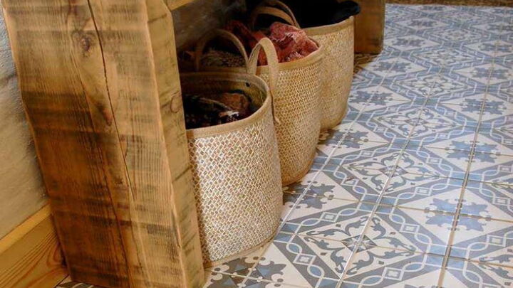 Gemusterte Bodenfliesen in Blau/Grün/Beige mit einem Ablagetisch aus Holz, darunter stehen Körbe
