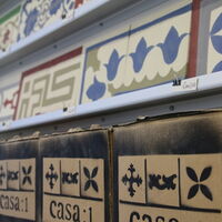 Regal mit einer Auswahl an Zementfliesen, darunter stehen Kartons mit der Aufschrift casa:1