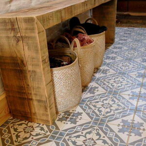 Gemusterte Bodenfliesen in Blau/Grün/Beige mit einem Ablagetisch aus Holz, darunter stehen Körbe