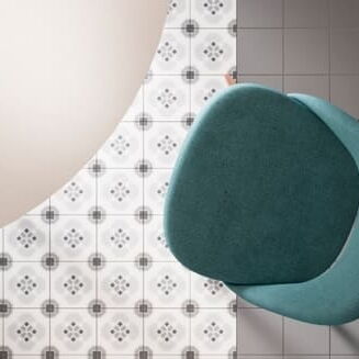 Bodenfliesen Grau-Weiß mit Dekor und unifarben; darauf steht ein türkisfarbener Stuhl und ein runder Tisch