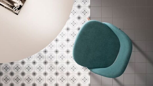 Bodenfliesen Grau-Weiß mit Dekor und unifarben; darauf steht ein türkisfarbener Stuhl und ein runder Tisch